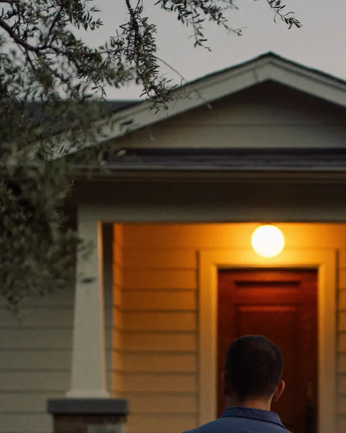 A service technician walks up to a house at dusk with the porch light on